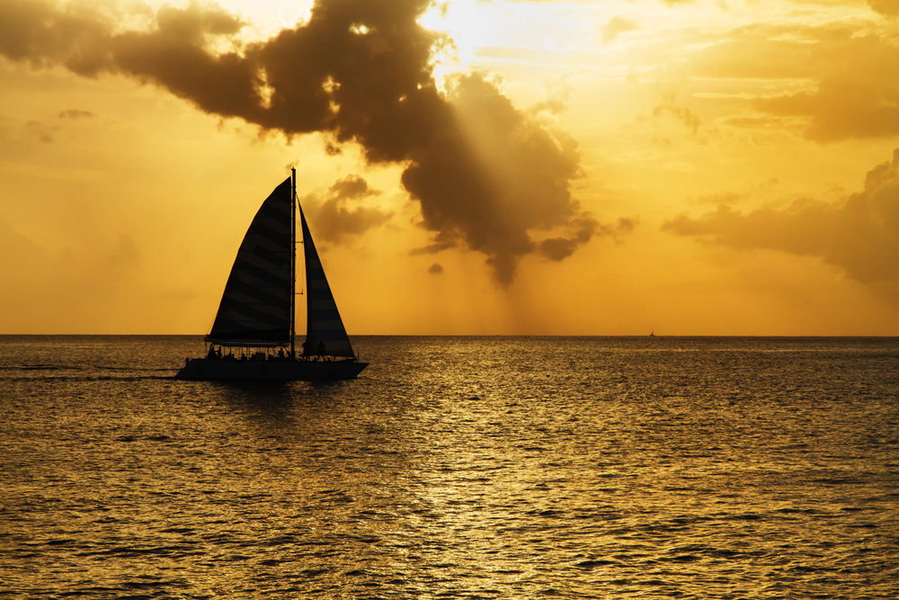 Image of a sailboat with a copper-colored sunset behind it